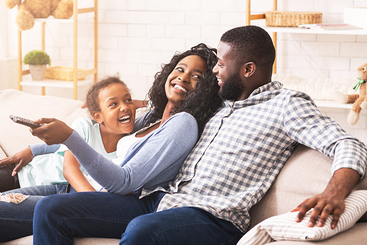 Family Sitting on Couch with TV Remote Smiling