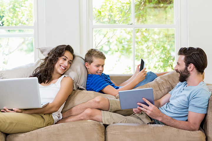 A family on their couch using internet on a laptop, mobile phone, and tablet